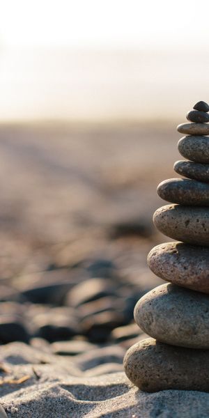 Serene HD phone wallpaper featuring a zen stone tower on a sunny beach