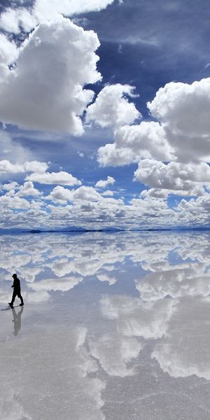 A Solitary Figure Walking on a Reflective Salt Flat Under Dramatic Clouds