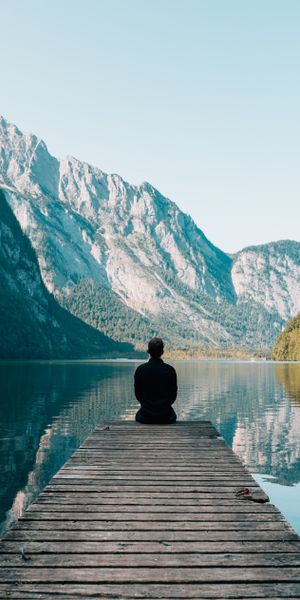 Tranquil Nature Wallpaper: A Person on a Wharf Surrounded by Mountains