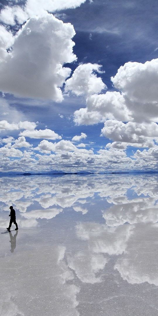 A Solitary Figure Walking on a Reflective Salt Flat Under Dramatic Clouds